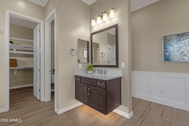 bathroom with wood finish floors, crown molding, a decorative wall, wainscoting, and vanity