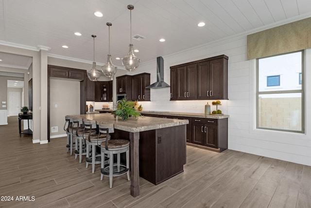 kitchen featuring ornamental molding, wall chimney range hood, dark brown cabinets, and light wood finished floors