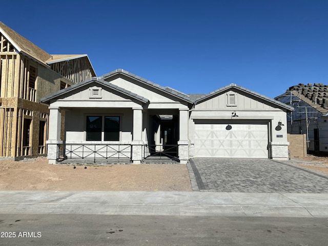 modern farmhouse style home with an attached garage, covered porch, a tile roof, and decorative driveway