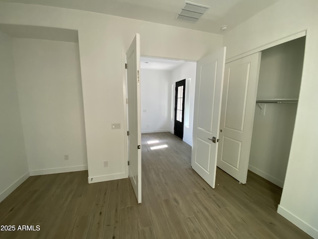 unfurnished bedroom featuring baseboards, a closet, visible vents, and wood finished floors