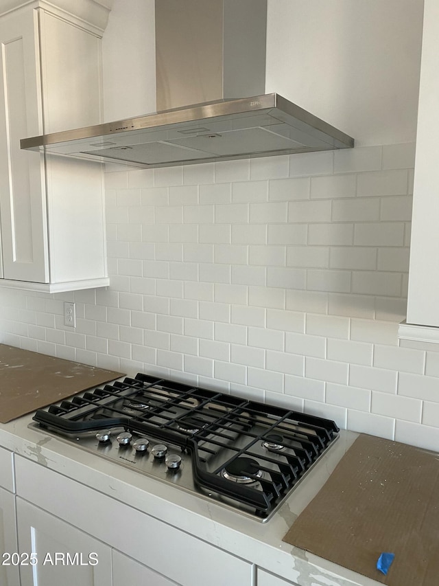 details featuring stainless steel gas stovetop, decorative backsplash, white cabinets, light stone countertops, and wall chimney exhaust hood