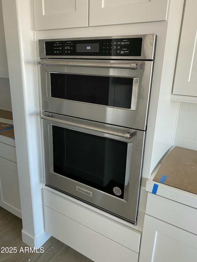 interior details with dark hardwood / wood-style floors, backsplash, white cabinets, and double oven