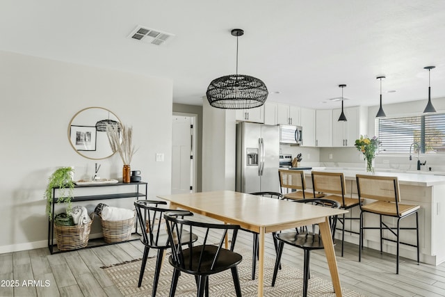 dining space with light wood finished floors, baseboards, and visible vents