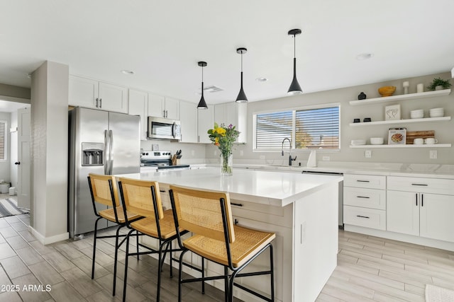 kitchen with light countertops, appliances with stainless steel finishes, a center island, open shelves, and a kitchen bar