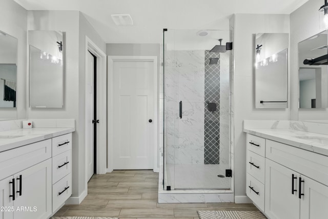 full bathroom with wood finish floors, a stall shower, two vanities, and baseboards