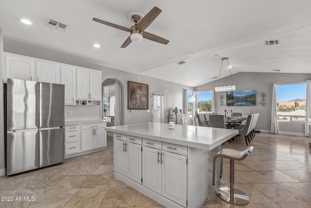 kitchen with vaulted ceiling, a kitchen island, white cabinets, stainless steel refrigerator, and hanging light fixtures