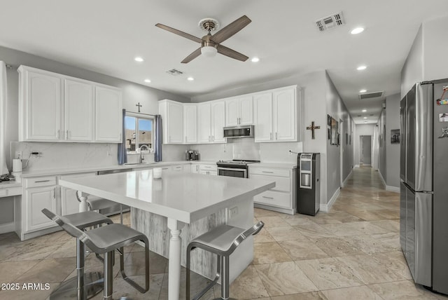 kitchen featuring white cabinetry, sink, ceiling fan, stainless steel appliances, and a breakfast bar area