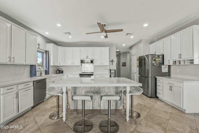 kitchen with a center island, sink, appliances with stainless steel finishes, white cabinetry, and a breakfast bar area