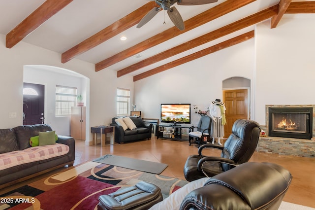 living area featuring arched walkways, high vaulted ceiling, a warm lit fireplace, ceiling fan, and beam ceiling