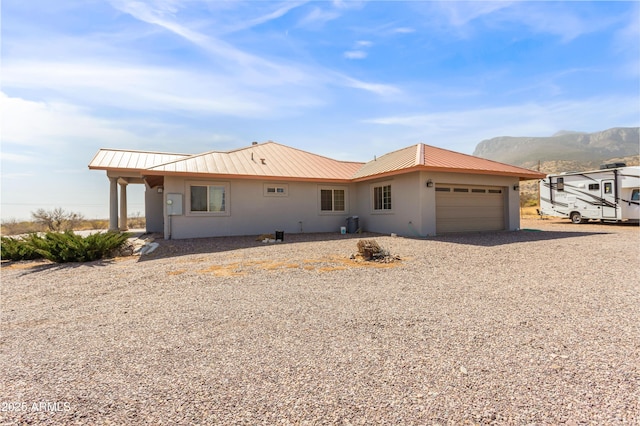 ranch-style house with gravel driveway, stucco siding, an attached garage, a mountain view, and metal roof