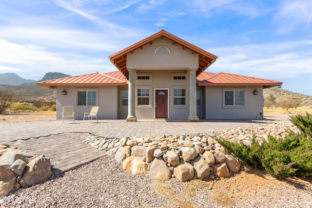 back of house featuring metal roof, a patio area, a mountain view, and stucco siding