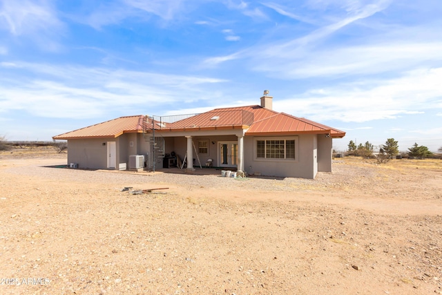 rear view of property with stucco siding, metal roof, a chimney, and central AC unit