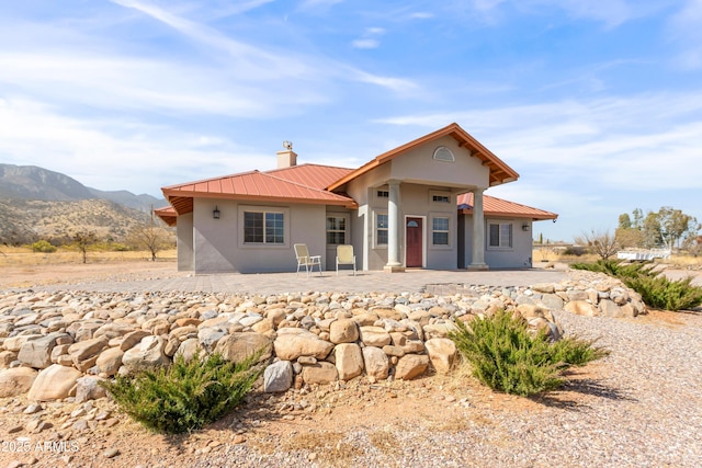 back of house with metal roof, a mountain view, stucco siding, a chimney, and a patio area