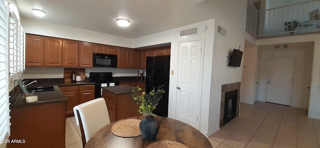 kitchen with black appliances, a sink, dark countertops, light tile patterned flooring, and a kitchen island