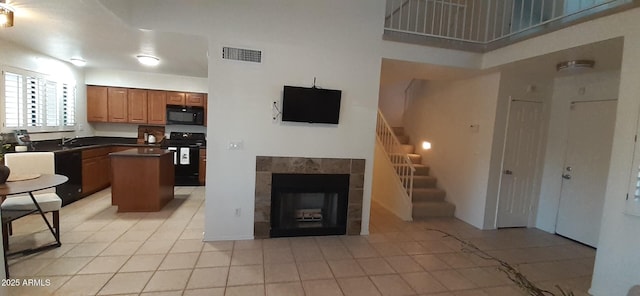 kitchen with black appliances, dark countertops, a kitchen island, a sink, and light tile patterned floors