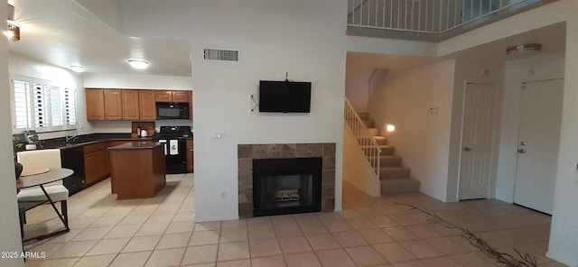 kitchen with black appliances, a sink, dark countertops, light tile patterned flooring, and a tile fireplace
