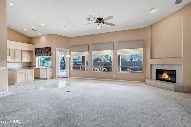 unfurnished living room featuring ceiling fan, high vaulted ceiling, light colored carpet, and a tiled fireplace