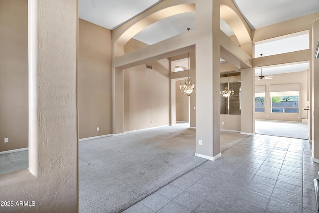 carpeted empty room featuring ceiling fan with notable chandelier and a towering ceiling