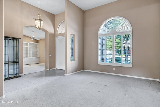 carpeted empty room with ceiling fan and a high ceiling