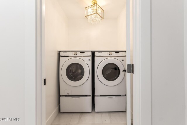 laundry area featuring light tile patterned flooring, washer and clothes dryer, and a chandelier