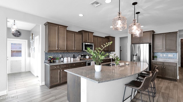 kitchen featuring light stone countertops, backsplash, stainless steel appliances, sink, and hanging light fixtures