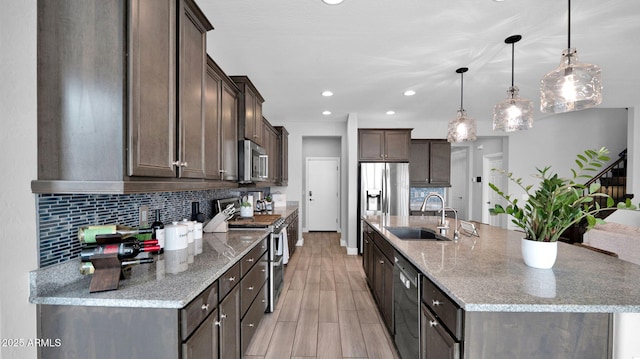 kitchen featuring dark brown cabinetry, light stone countertops, sink, pendant lighting, and appliances with stainless steel finishes