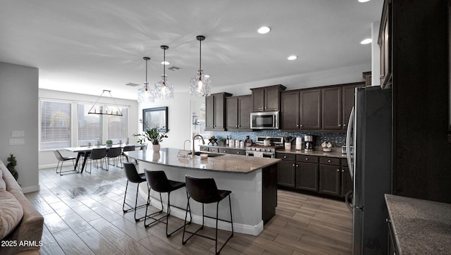 kitchen featuring sink, tasteful backsplash, an island with sink, a kitchen bar, and appliances with stainless steel finishes