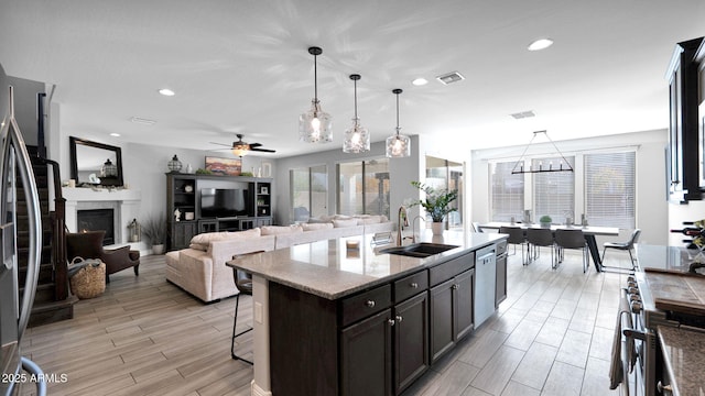 kitchen featuring light stone counters, stainless steel appliances, sink, pendant lighting, and a center island with sink