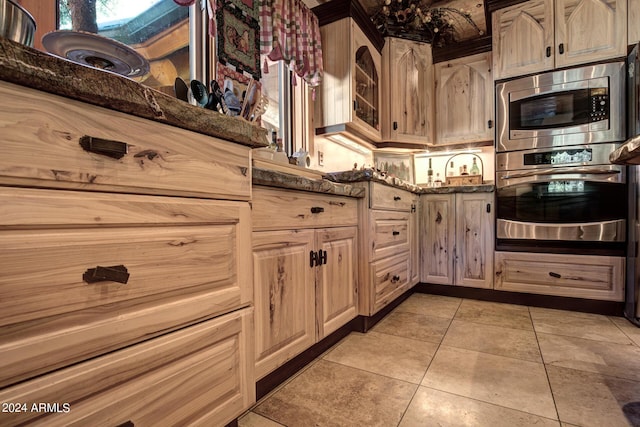 kitchen with light tile patterned floors, stainless steel appliances, glass insert cabinets, and dark stone countertops