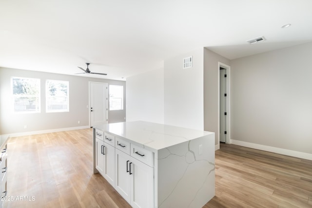 kitchen featuring white cabinets, a center island, ceiling fan, light stone countertops, and light hardwood / wood-style flooring