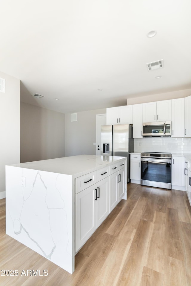 kitchen with appliances with stainless steel finishes, white cabinetry, tasteful backsplash, light hardwood / wood-style floors, and a kitchen island