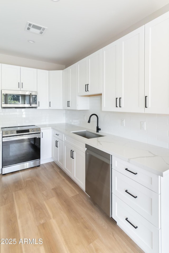 kitchen with sink, light stone counters, light hardwood / wood-style flooring, appliances with stainless steel finishes, and white cabinets