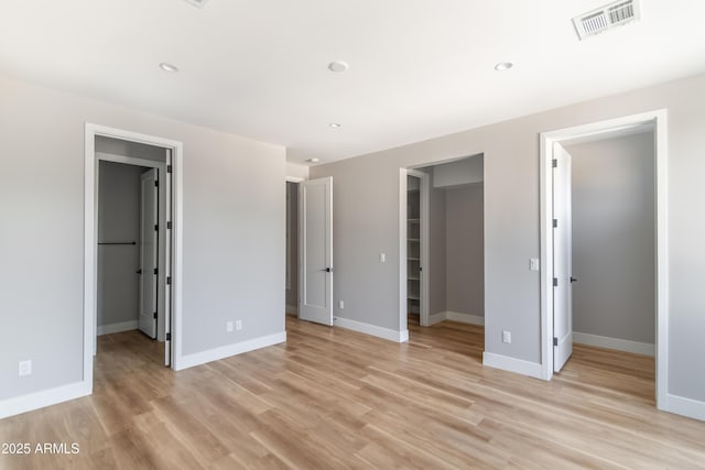 unfurnished bedroom with light wood-type flooring, a spacious closet, ensuite bath, and a closet