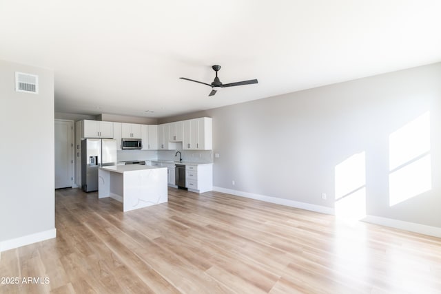 kitchen with tasteful backsplash, appliances with stainless steel finishes, a kitchen island, ceiling fan, and white cabinets