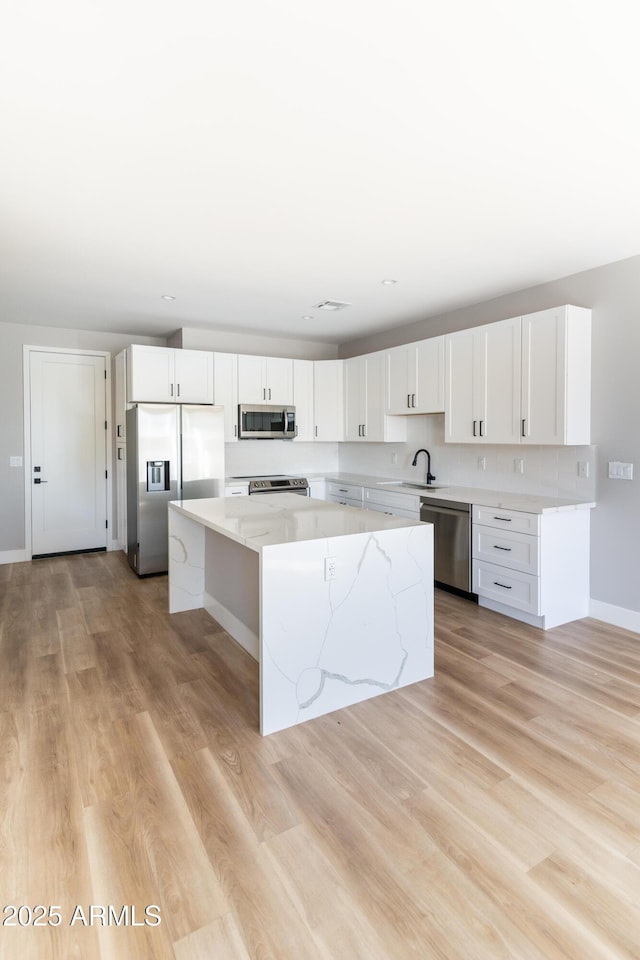 kitchen featuring appliances with stainless steel finishes, white cabinetry, sink, a center island, and light hardwood / wood-style flooring