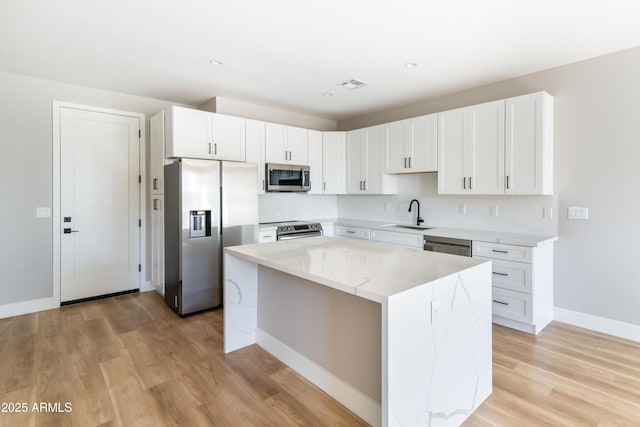 kitchen featuring sink, white cabinetry, light stone counters, a center island, and stainless steel appliances