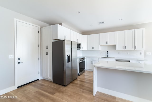 kitchen with appliances with stainless steel finishes, sink, white cabinets, light stone countertops, and light hardwood / wood-style flooring