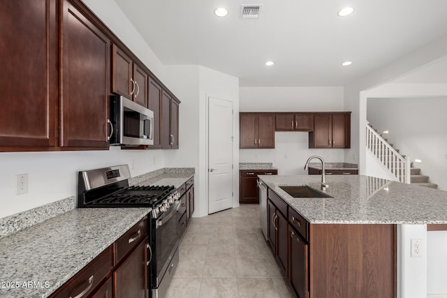 kitchen featuring visible vents, a sink, light stone counters, stainless steel appliances, and a kitchen island with sink