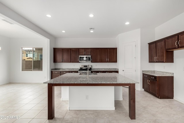 kitchen with visible vents, an island with sink, a kitchen bar, light stone counters, and appliances with stainless steel finishes