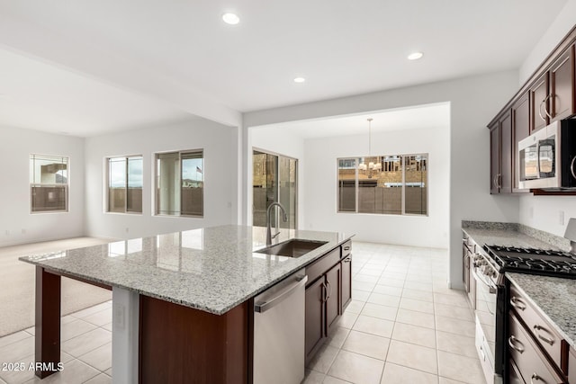 kitchen with light tile patterned floors, light stone countertops, a center island with sink, a sink, and stainless steel appliances