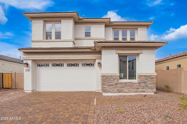 prairie-style home featuring stucco siding, decorative driveway, stone siding, fence, and an attached garage