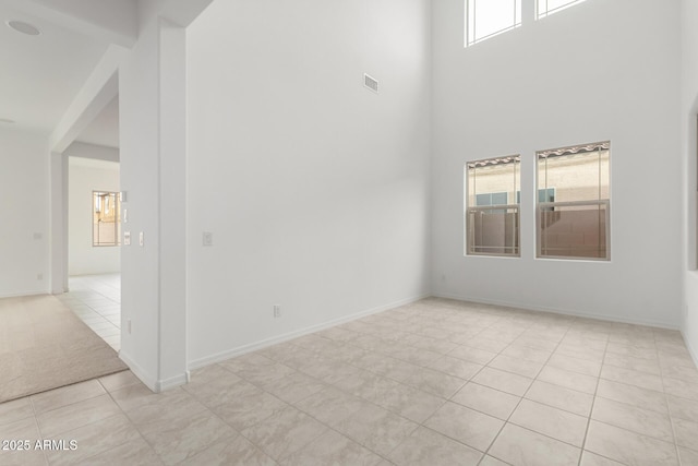 spare room featuring a high ceiling, light tile patterned floors, baseboards, and visible vents