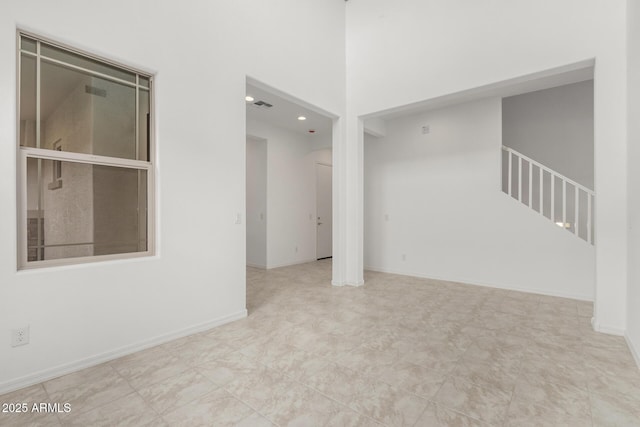 spare room featuring visible vents, a high ceiling, stairs, and baseboards