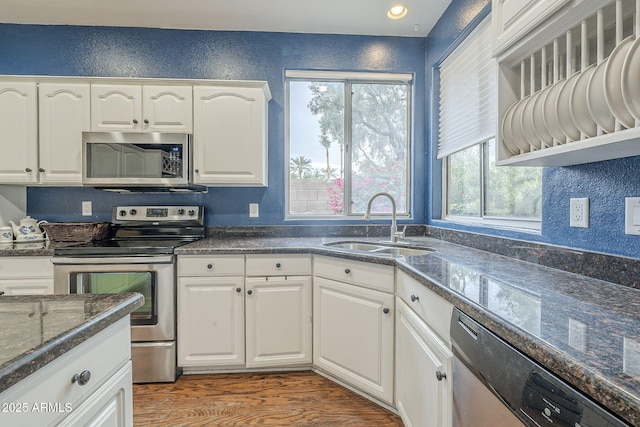 kitchen featuring stainless steel appliances, a sink, white cabinets, wood finished floors, and dark stone countertops