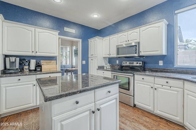 kitchen featuring stainless steel appliances, a textured wall, light wood-style floors, white cabinets, and a center island