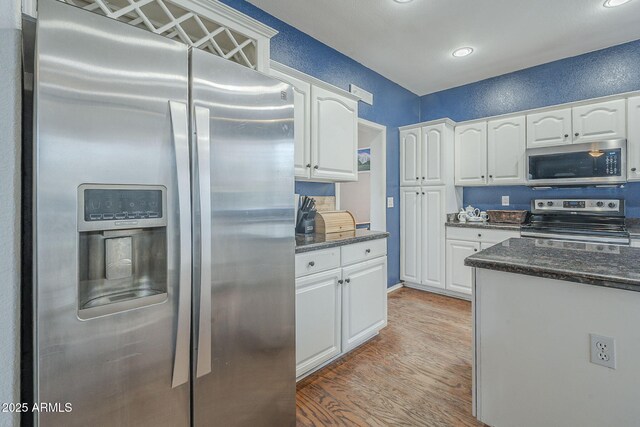 kitchen featuring stainless steel appliances, white cabinets, light wood finished floors, dark stone counters, and recessed lighting