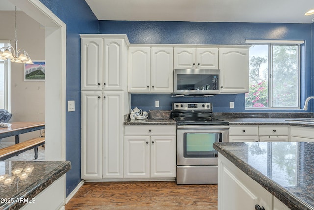 kitchen with appliances with stainless steel finishes, a chandelier, wood finished floors, and white cabinets