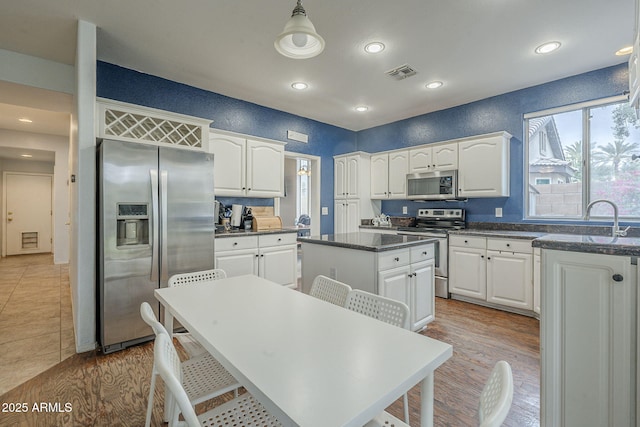 kitchen with appliances with stainless steel finishes, a kitchen island, a sink, white cabinets, and recessed lighting
