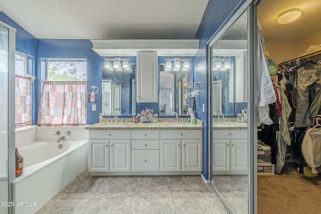 bathroom with double vanity, a walk in closet, a garden tub, and a chandelier