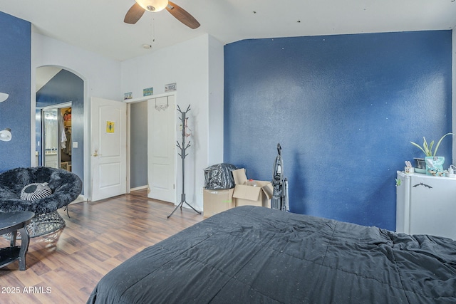 bedroom with arched walkways, wood finished floors, lofted ceiling, and ceiling fan
